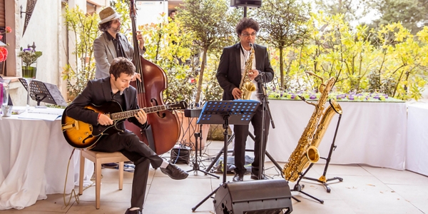 Un groupe d'artistes jazz propose un concert sur mesure en extérieur avec une formation trio saxophoniste, guitariste et contrebassiste.