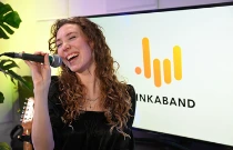 Une chanteuse se tient devant un micro en train de chanter sur scène, elle a le bras levé et la main sur le coeur.