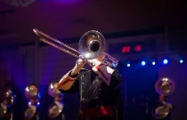 Une fanfare joue dans la rue, c'est une animation musicale mobile où l'on voit cinq joueurs de cuivres devant un ciel bleu.
