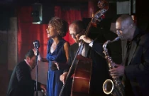 Groupe de jazz jouant un concert. Il est composé d'une chanteuse, d'un contrebassiste et d'un saxophoniste.