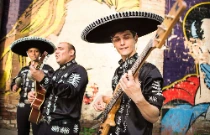Groupe Latino en tenue traditionnelle de mariachi mexicain, jouant dans la rue devant un mur peint de la guitare.