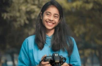 Photographe souriant regardant vers le côté et tenant un appareil photo reflex dans les mains