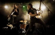 Groupe de Rock qui joue un concert sur scène avec le trio classique du rock : guitariste, bassiste et batteur se tenant devant des projecteurs.